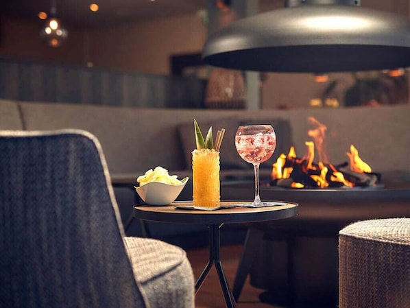 A cozy seating area with a round table featuring a drink and a candle, a bowl of snacks, and a fire pit in the background. - Stay on Ameland Near Beach – Hotel Comfort, Dining & Nature Walks - 4 Units (Nes)