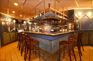 Zona de bar con barra central, varios taburetes y estantes llenos de botellas.