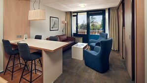 A hotel room with a wooden desk, two blue chairs, a brown sofa, and a view of the outdoors through a large window. - North Sea Getaway – Hotel Near Dunes, Beach Trails & Ferry Port - 2 Units (Nes)