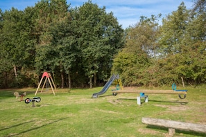 Un parque infantil con columpios, tobogán y balancín.