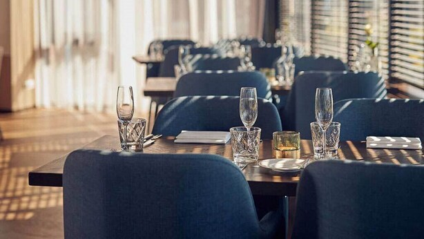 A restaurant with tables set for dining, featuring blue upholstered chairs and clear glassware. - North Sea Getaway – Hotel Near Dunes, Beach Trails & Ferry Port - 2 Units (Nes)