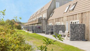 A row of wooden cabins with stone walls, outdoor seating, and a grassy pathway. - North Sea Getaway – Hotel Near Dunes, Beach Trails & Ferry Port - 2 Units (Nes)