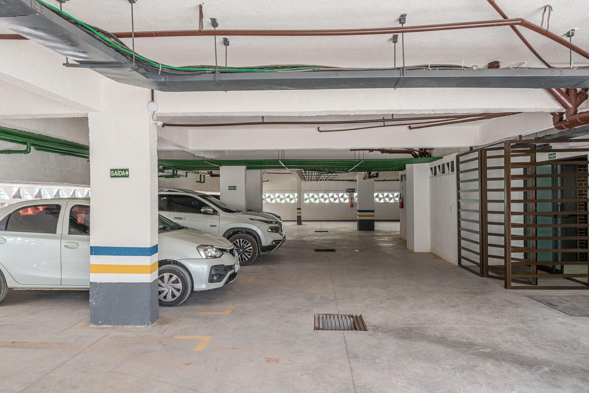 Un estacionamiento con varios autos estacionados, pisos de concreto y elementos estructurales visibles como columnas y tuberías.