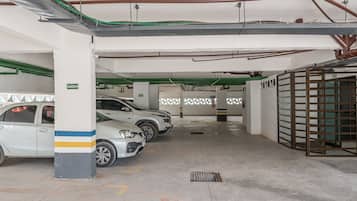Un estacionamiento con varios autos estacionados, pisos de concreto y elementos estructurales visibles como columnas y tuberías.