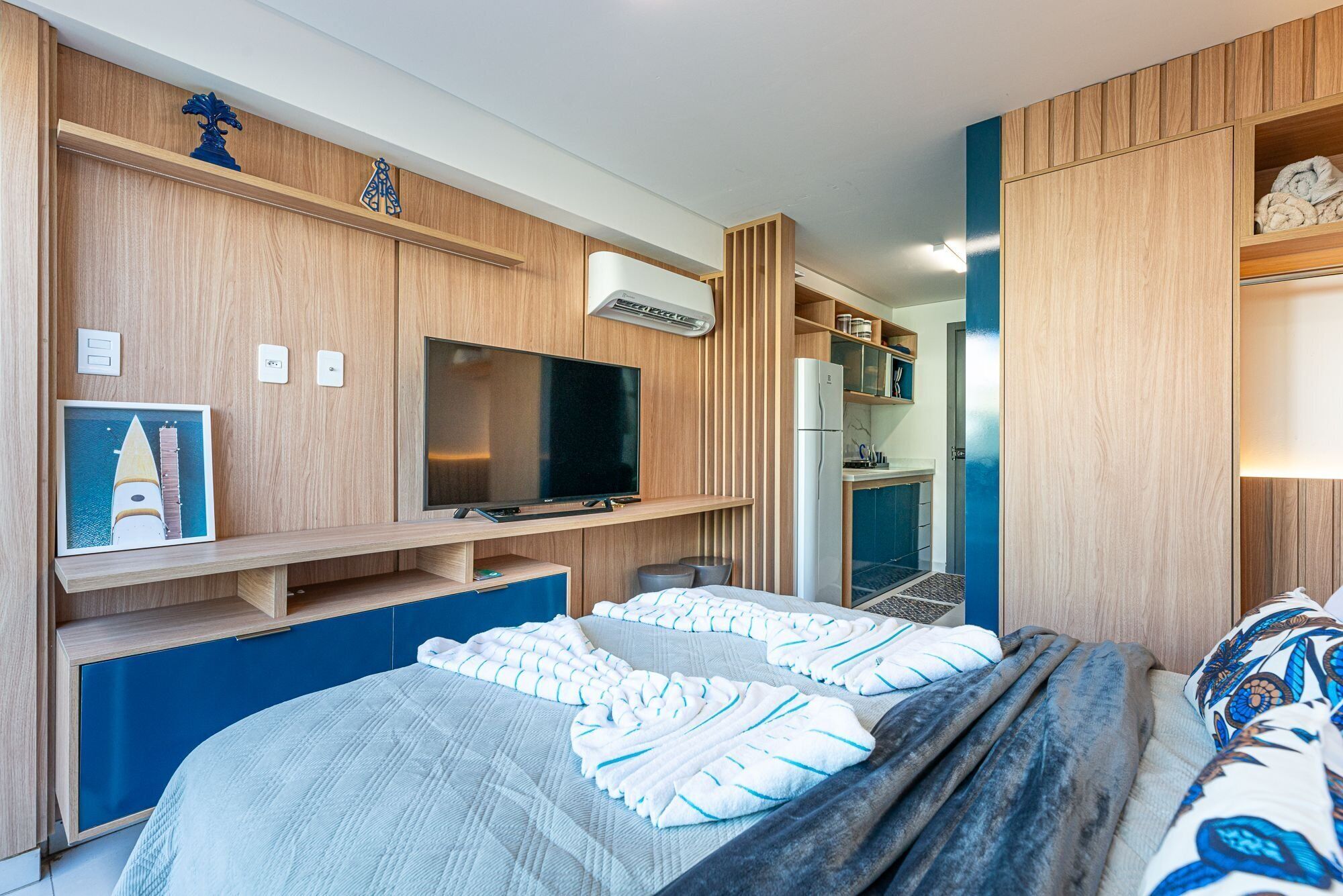 Quarto moderno com cama, televisão, frigorífico e uma área de kitchenette.