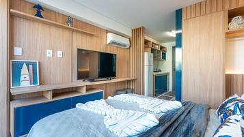 Quarto moderno com cama, televisão, frigorífico e uma área de kitchenette.