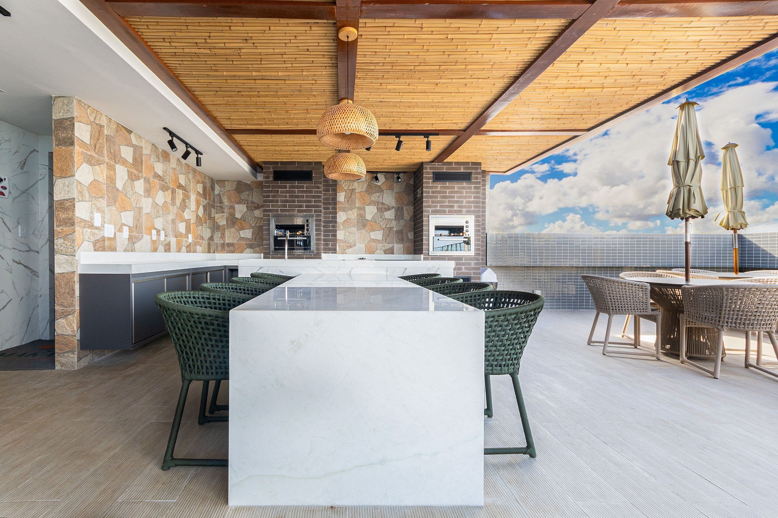 Cocina moderna con una isla grande, salpicadero de piedra y zona de estar al aire libre con sillas de mimbre y sombrillas.