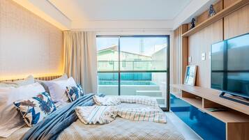 Habitación de hotel con cama, televisión, ventana y balcón con vista a edificios.