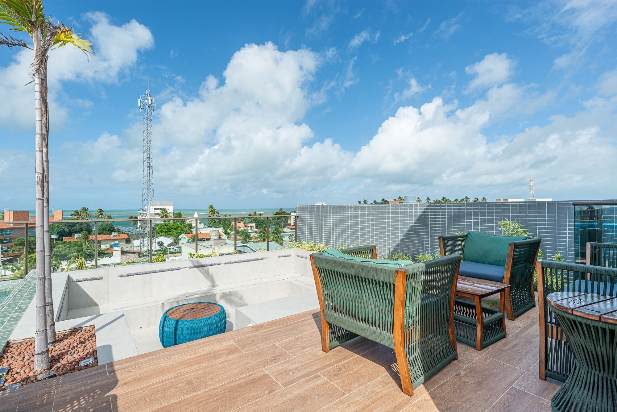 A rooftop terrace with outdoor furniture, a palm tree, and a view of the cityscape and ocean.