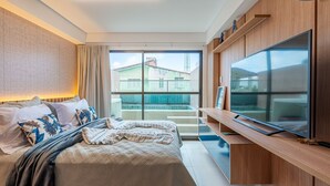 Habitación de hotel con cama, televisión, balcón y vistas a edificios.