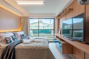 Ein Hotelzimmer mit Bett, Fernseher, Balkon und Blick auf Gebäude sowie einem Fenster.