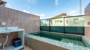 A rooftop swimming pool with a view of a residential area, a water filtration system, and a storage box.