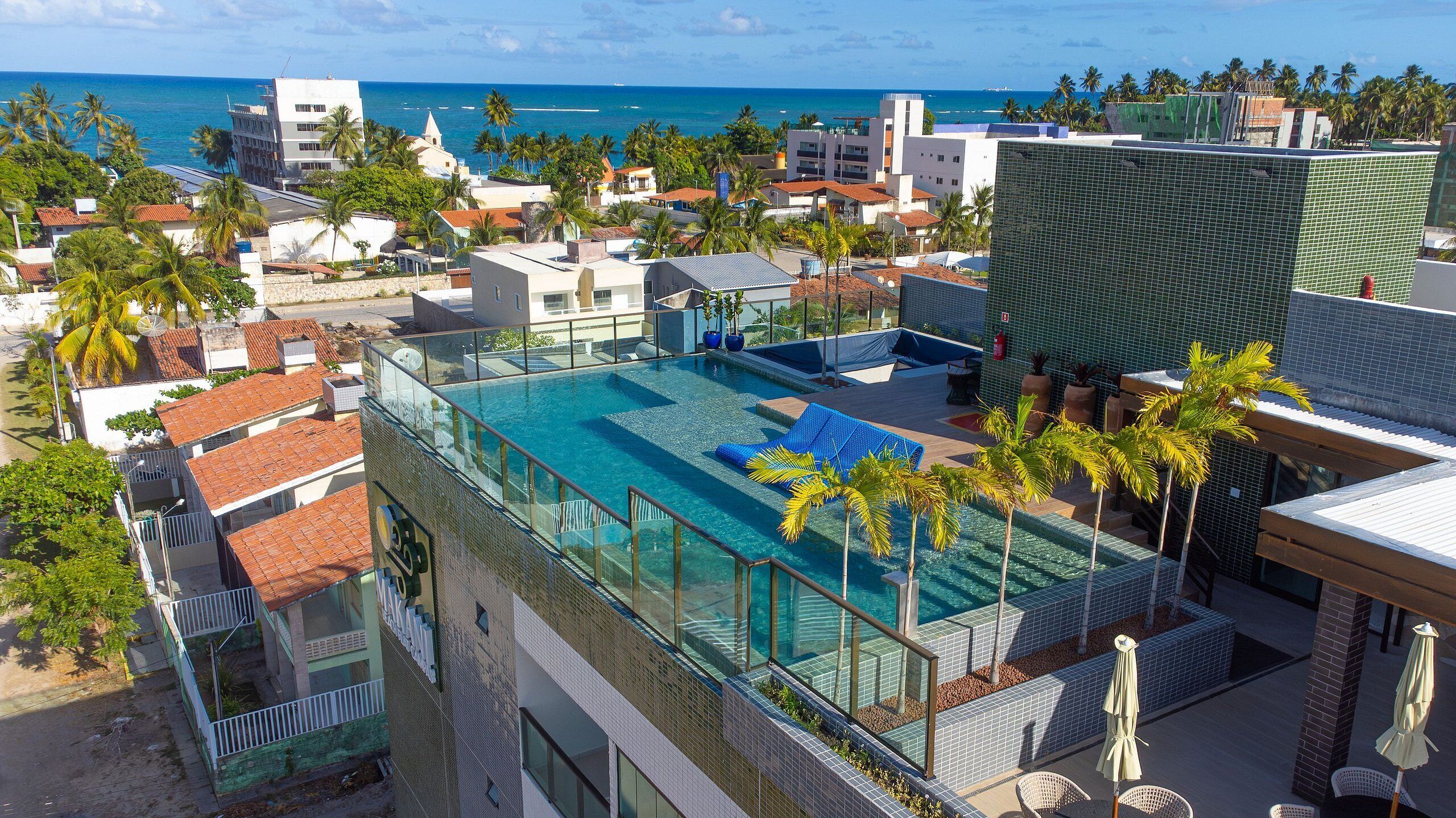 Una piscina en la azotea con agua cristalina, rodeada de palmeras y edificios modernos.
