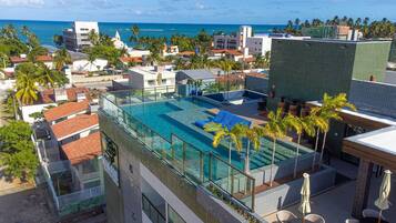 Una piscina en la azotea con agua cristalina, rodeada de palmeras y edificios modernos.