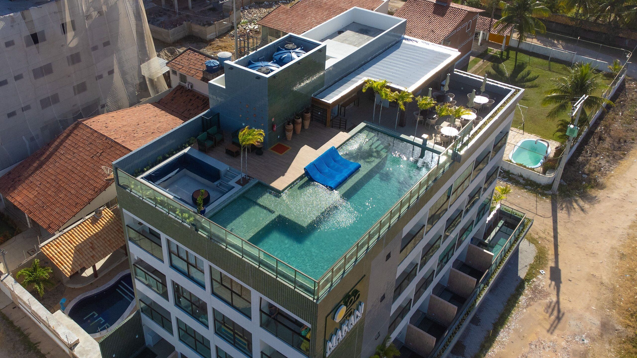Un hotel moderno con piscina infinita en la azotea, zona de estar techada al aire libre y vistas del barrio circundante.