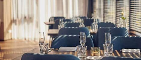 Un restaurante con mesas dispuestas para comer, con sillas tapizadas en azul y copas de cristal transparente.