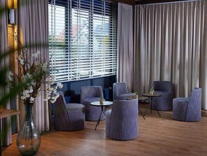 Una habitación moderna con un ventanal amplio, varios rincones de estar redondos y un jarrón con flores.
