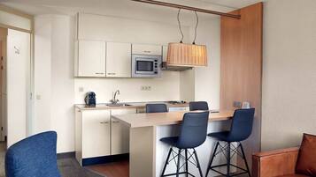 A compact kitchen with a microwave, a hanging light fixture, and a small island with bar stools.
