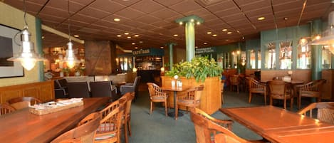A restaurant with wooden tables and chairs, a bar area, and a green plant centerpiece.