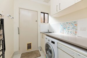 Een wasserette met een wasmachine, een wasbak en een deur.