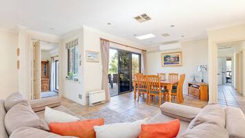 A spacious living area with a sofa, a dining table with chairs, and a view through a glass door to an outdoor patio.