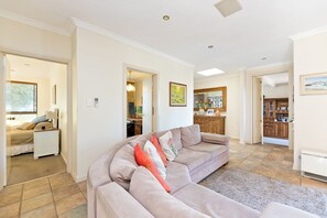 A living room with a sofa, a rug, and a kitchen area visible through an open doorway. - Comfortable 4-bedroom fully-furnished home near train & Carine Open Space (Duncraig)