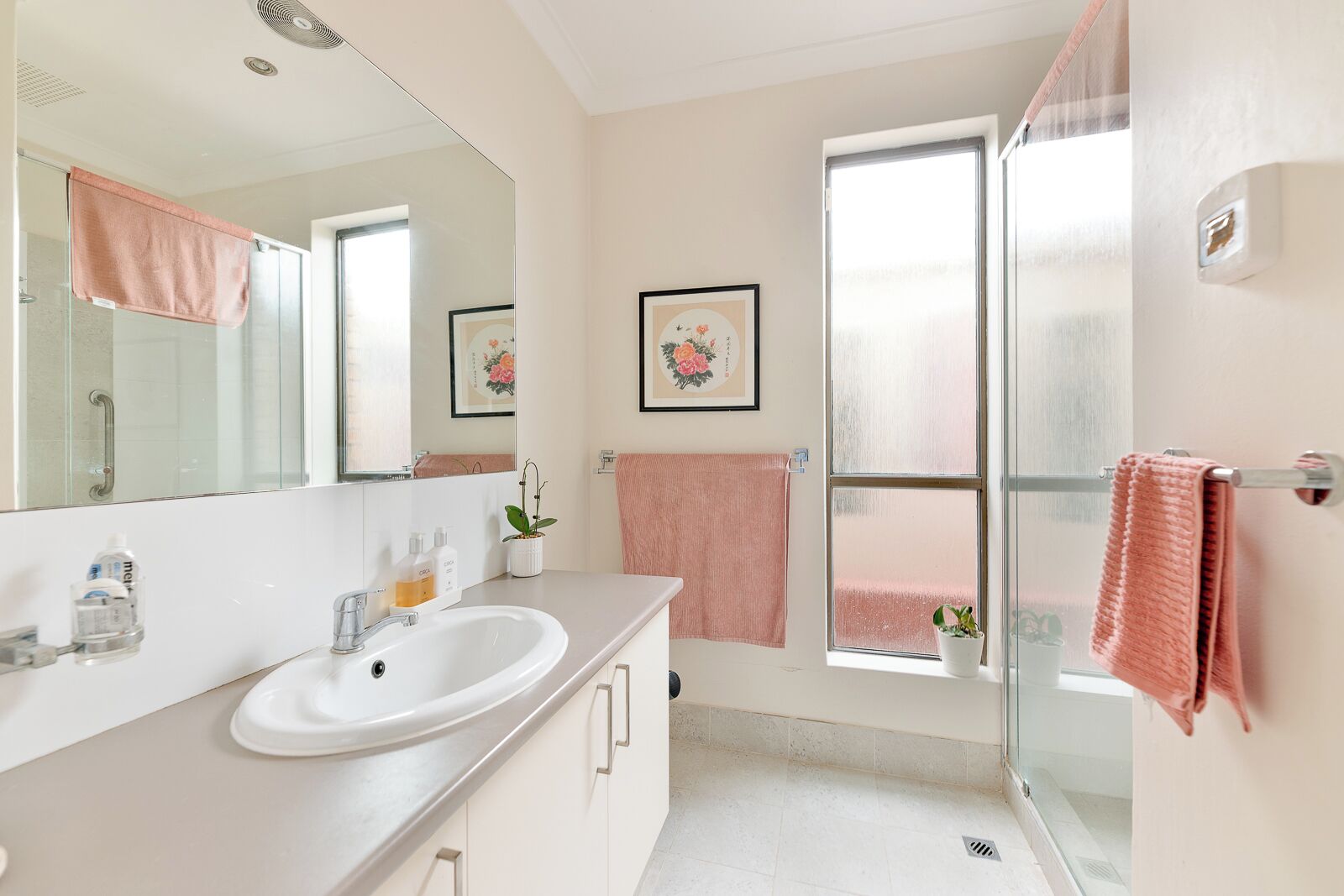 Een badkamer met een witte wastafel, een spiegel, een douche en een raam.