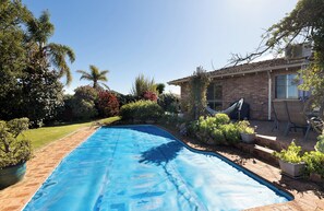 Ein Swimmingpool mit blauer Abdeckung, umgeben von einer Ziegelterrasse, einer Hängematte und einem Ziegelhaus mit Fenster.