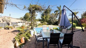 Una terrazza esterna con tavolo e sedie, circondata da piante in vaso e vista su una piscina.