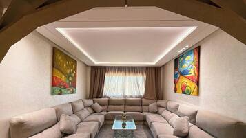 A modern living room with a sectional sofa, a glass coffee table, and two large paintings on the walls.