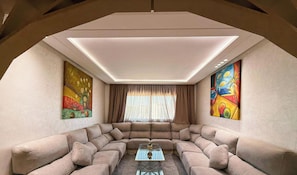 A modern living room with a sectional sofa, a glass coffee table, and two large paintings on the walls.