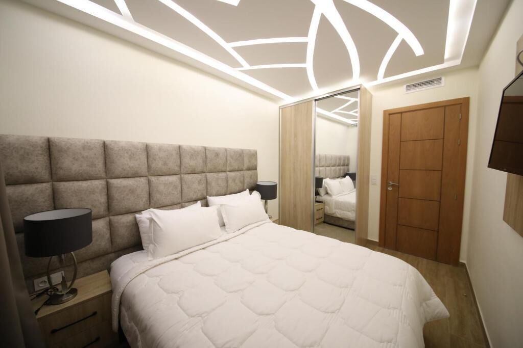 A bedroom with a large bed, a headboard, bedside lamps, a wardrobe, and a mirror.