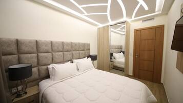 A bedroom with a large bed, a headboard, bedside lamps, a wardrobe, and a mirror.