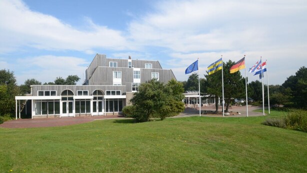 En moderne bygning med stor glassefterdør, omgivet af en velplejet græsplæne og flere nationalflag.
