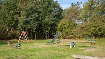 Une aire de jeux avec des balançoires, un toboggan et une bascule.