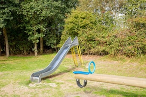 A playground with a slide and swings in a park. - Island Comfort Steps from Ameland Beach, Dunes & Ferry – Hotel w/ Parking (Nes)