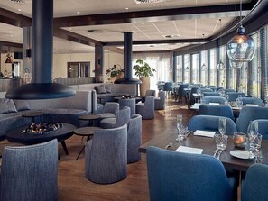 En moderne restaurant med runde borde, bløde blå stole og en central pejs.