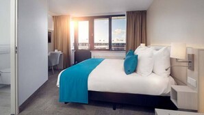 Et hotelværelse med en stor seng, et skrivebord og udsigt over byen.