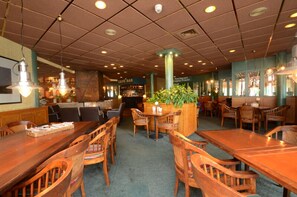 Un restaurante con mesas y sillas de madera, una zona de bar y un centro de mesa con planta verde.