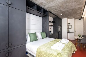 Ett modernt hotellrum med en säng, ett litet pentry, en matplats och ett badrum.