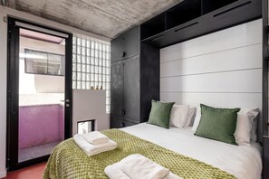 Ett modernt hotellrum med en säng, en garderob, ett fönster med utsikt och en dörr som leder ut till ett utomhusområde.