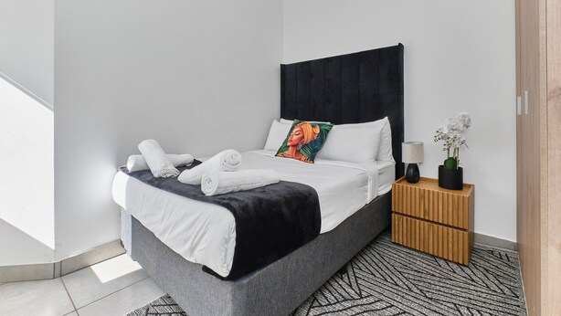 A modern bedroom with a bed, pillows, a bedside table, and a nightstand. - Luxury Living in Circa Illovo by Ctha (Johannesburg)