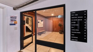 An interior space with a glass door leading to a lobby area, a sign listing various rooms and amenities, and a poster on the wall. - Luxury Living in Circa Illovo by Ctha (Johannesburg)