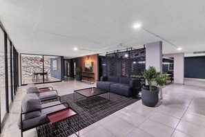 A modern lounge area with a sectional sofa, a coffee table, and a potted plant. - Luxury Living in Circa Illovo by Ctha (Johannesburg)
