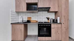 A compact kitchen with wooden cabinetry, a microwave, a stove, and an oven. - Luxury Living in Circa Illovo by Ctha (Johannesburg)
