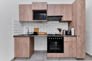 A compact kitchen with wooden cabinetry, a microwave, a stove, and an oven. - Luxury Living in Circa Illovo by Ctha (Johannesburg)