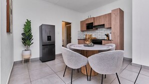 A compact kitchen with a central island, two chairs, a refrigerator, and wooden cabinets. - Luxury Living in Circa Illovo by Ctha (Johannesburg)
