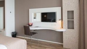 Et moderne hotelværelse med skrivebord i kurvet design, en stol, en lille skraldespand og et TV monteret på væggen.
