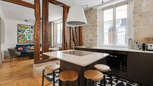 A modern kitchen with a central island, bar stools, and a stone wall. - A Stunning 2-BR in the 9th district- Folies (Paris)