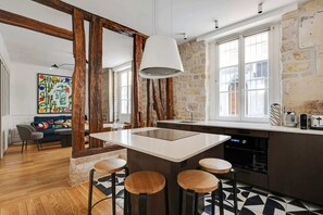 A modern kitchen with a central island, bar stools, and a stone wall. - A Stunning 2-BR in the 9th district- Folies (Paris)